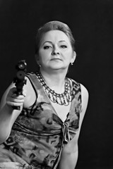 A middle aged, white, woman holds a semi automatic pistol with silencer and collimator against black
