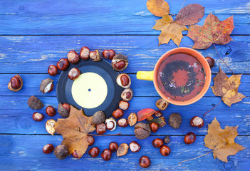 Yellow ceramic cup of herbal tea and vintage vinyl records on aged wooden background with fall autumn leaves and chestnuts.