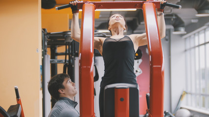 Fitness-club - young woman performs Pull-Ups with male coach