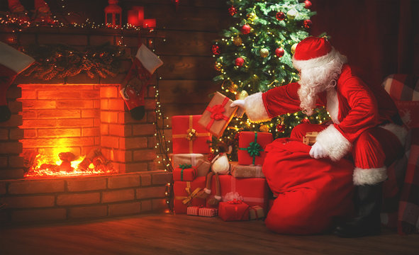 Merry Christmas! Santa Claus Near The Fireplace And Tree With Gifts