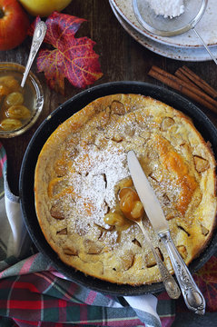American cuisine: apple Dutch baby lush omelet in frying pan, powdered sugar and green grapes jam dressing. Top view, rustic style