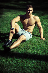 Man sportsman with muscular body sit on green grass