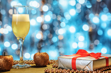 Christmas composition: a glass of champagne, gift, decor on a blurry, shiny background, free copy space