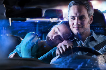 Man driving his car at night, his wife asleep on his shoulder.