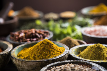 A selection of various colorful spices on a wooden table in bowls