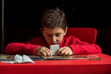 Boy sticking stickers in album on the table