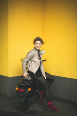 Fototapeta na wymiar stylish girl sits on a moped against the background of a yellow wall