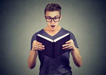 Surprised young man in glasses reading a book