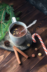 Cup of homemade hot chocolate with hazelnuts and cinnamon sticks on wooden table. Top view. Christmas holiday background. Cozy home scene. 