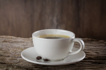 A cup of hot coffee on a wooden table with roasted coffee beans