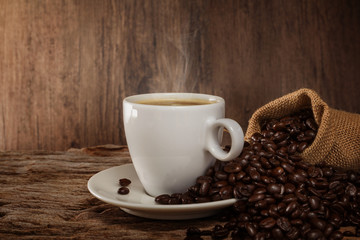 A cup of hot coffee on a wooden table with roasted coffee beans