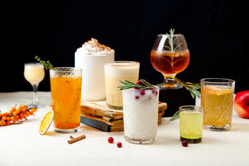 Set of various winter cocktails: mulled wine, eggnog, limoncello, old-fashioned, coconut margarita. Black background, white linen tablecloth.