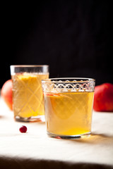 Two vintage glasses with apple cider on black background. Christmas beverages concept. Two red apples and rosemary sprig aside.  Warm backlight. Vertical composition.