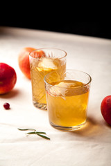 Two vintage glasses with apple cider on black background. Christmas beverages concept. Two red apples and rosemary sprig aside.  Warm backlight. Vertical composition.