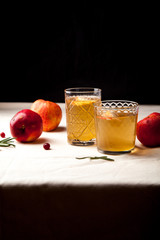 Two vintage glasses with apple cider on black background. Christmas beverages concept. Two red apples and rosemary sprig aside.  Warm backlight. Vertical composition.
