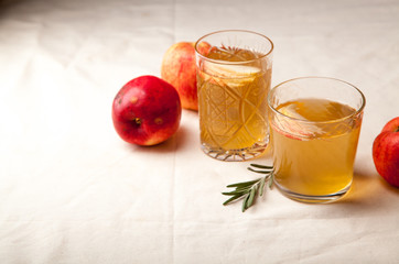 Two vintage glasses with apple cider on black background. Christmas beverages concept. Two red apples and rosemary sprig aside.  Warm backlight.