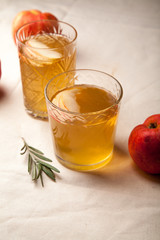 Two vintage glasses with apple cider on black background. Christmas beverages concept. Two red apples and rosemary sprig aside.  Warm backlight. Vertical composition.