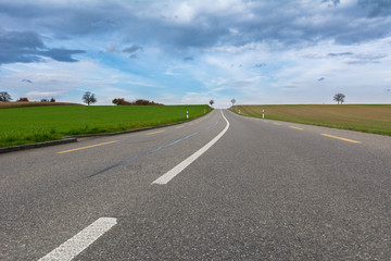 Strasse - Hauptstrasse mit grünem Feld und bewölktem Himmel