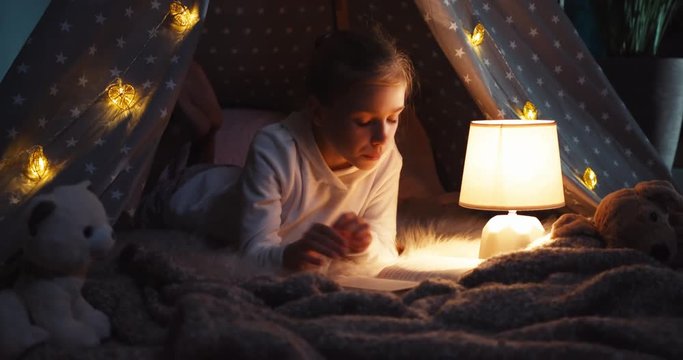 Girl child reading book at night in the wigwam. Slider shot