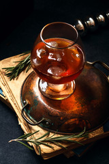 Whiskey cocktail with ice and burnt rosemary. Dark background, vintage papers, dramatic lighting....