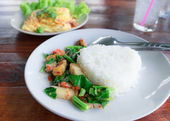 Close up view. Crispy Pork with Kale topped with rice in dish and Stuffed omelet. On the wooden table.