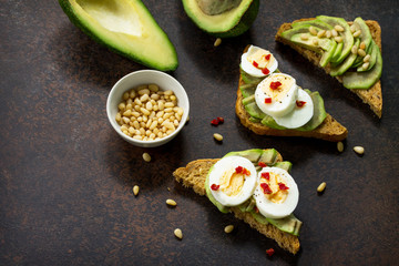 Sandwich avocado with fresh sliced avocado, egg poached and spices on a dark slate or stone background. Copy space. Flat lay, top view.