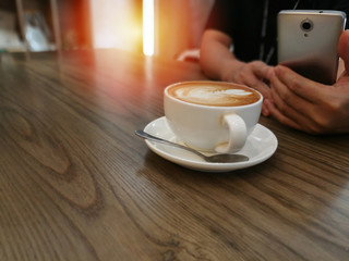 Top view latte art coffee on wooden table background and man using mobile phone in office