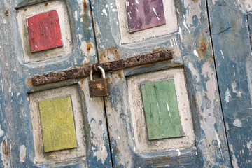 Brightly coloured flaky pain in blue, yellow, red, purple and green on old window shutters secured with a rusting bolt and padlock. Shot as a Dutch tilt in the Souk in Essaouira,Morocco