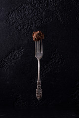 Candy truffle on a dessert fork levitating on a black background. Candy on a beautiful antique fork with a pattern. Homemade truffle crockery on a black background.