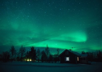 Northern lights (Aurora Borealis) over  cottage in Lapland village. Finland