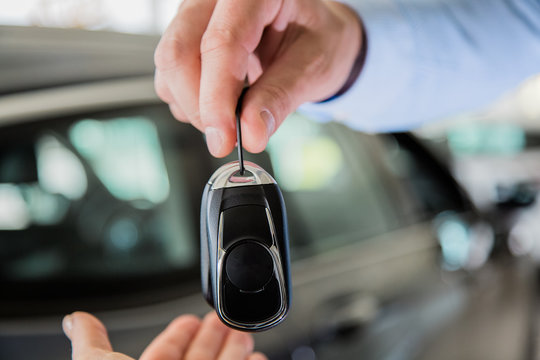 close up photo of male hand giving car keys to female hand, indoors in car dealership