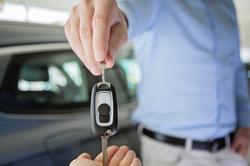 close up photo of male hand giving car keys to female hand, indoors in car dealership