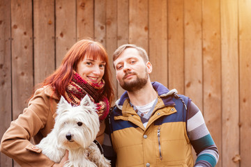 Close up portrait of happy young family with a white dog with wooden plank on background. Love and friendship concept