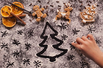 Child hand drawing holidays scene in the flour prepared for the christmas cookies