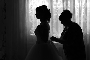 Bride getting dressed by her mother. On the wedding day at the window, my mother laces up the dress of the daughter of the bride