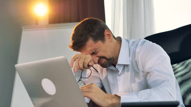 A tired businessman types on a laptop. 