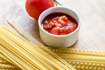 Dry spaghetti, fresh tomato and tomato sauce, closeup. Ingredients of Italian pasta meal, wooden background, high angle.