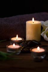 Fototapeta na wymiar A candle in a glass vase, decoration and various interesting elements on a dark wooden background. Candles burning. Set for spa and massage. stones for massage