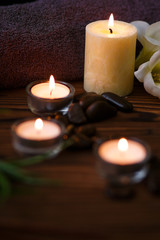 A candle in a glass vase, decoration and various interesting elements on a dark wooden background. Candles burning. Set for spa and massage. stones for massage