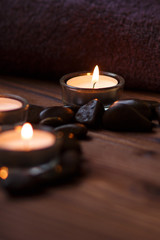 A candle in a glass vase, decoration and various interesting elements on a dark wooden background. Candles burning. Set for spa and massage. stones for massage