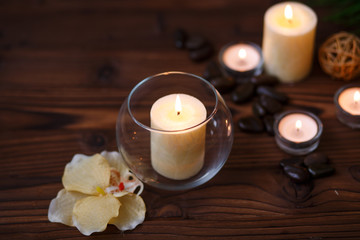 A candle in a glass vase, decoration and various interesting elements on a dark wooden background. Candles burning. Set for spa and massage. stones for massage