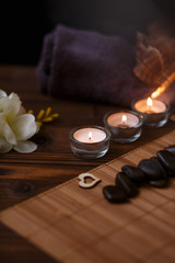 A candle in a glass vase, decoration and various interesting elements on a dark wooden background. Candles burning. Set for spa and massage. stones for massage