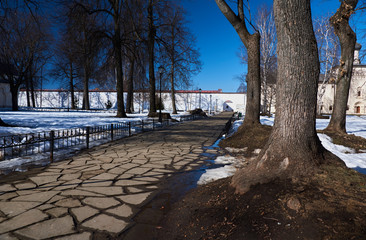 In the Orthodox monastery/City landscape of Suzdal. Vintage monastery. Inside the monastery a path of slabs, a metal fence and trees along the path. Suzdal.Golden Ring of Russia