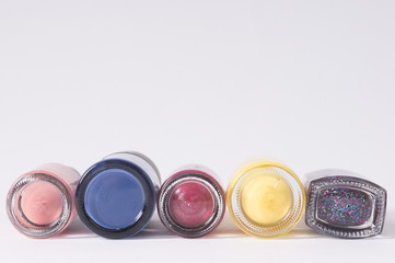 many colored bottles of nail polish in a row, closeup on white background bottom view