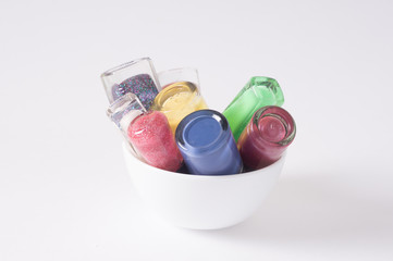 many colored bottles of nail polish in cup closeup on white background bottom view