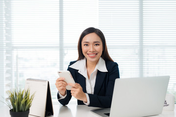 Asian businesswoman holding smartphone while sitting at her desk