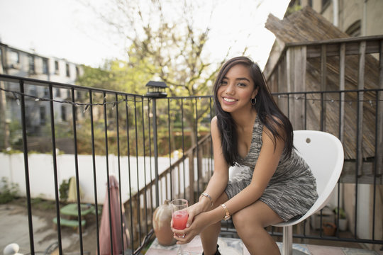 Portrait of young woman with cocktail glass sitting on chair