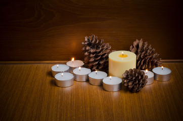 Obraz na płótnie Canvas Lid yellow and white candles with pine cones over teak wood table and wall background at night time with copy space for text or wordings decoration, warm xmas or special event celebration concept