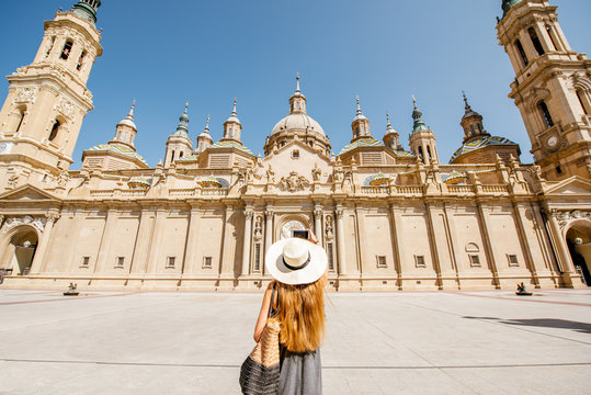 Young woman tourist in sunhat standing back in front of the famous cathedral on the central square during the sunny weather in Zaragoza city, Spain