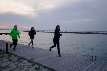 group of young people training outdoors, runners exercises, sea or river background 